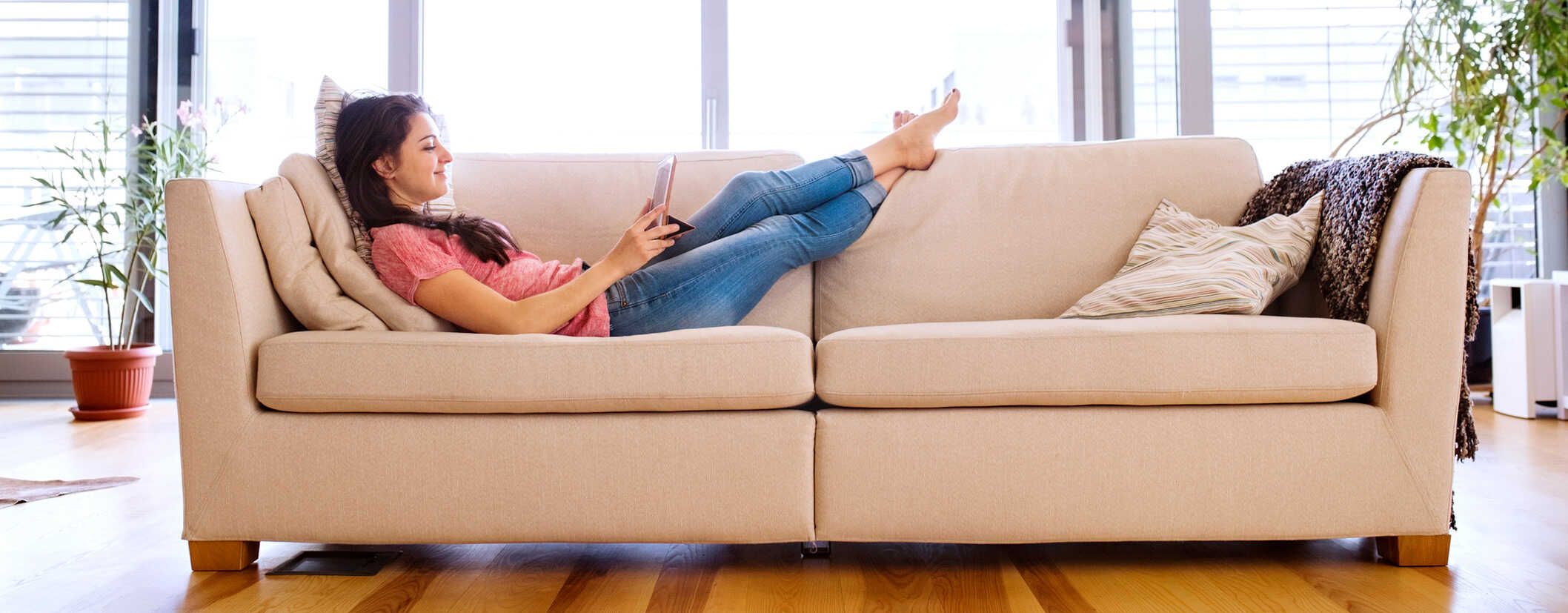 Woman on her couch reading on a digital tablet.
