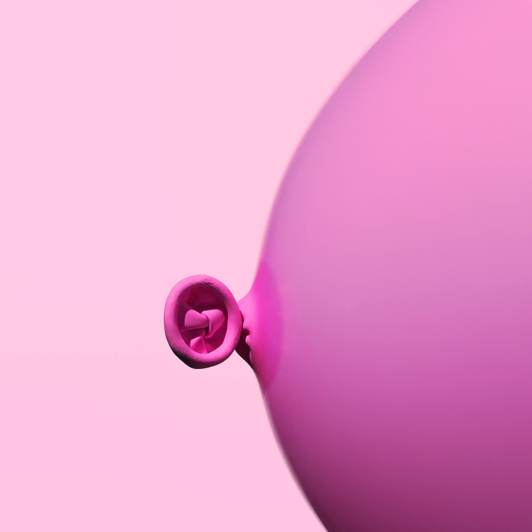 pink background with a pink balloon. you just see half of the balloon from the side. it's the knot. it's used to represent a breast