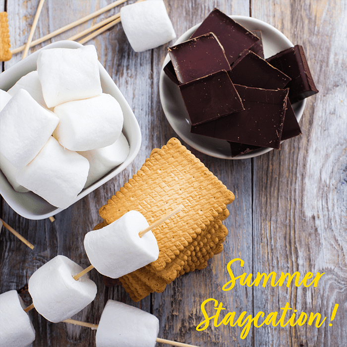 Bowl of chocolate squares, skewers of marshmallows and a stack for graham crackers