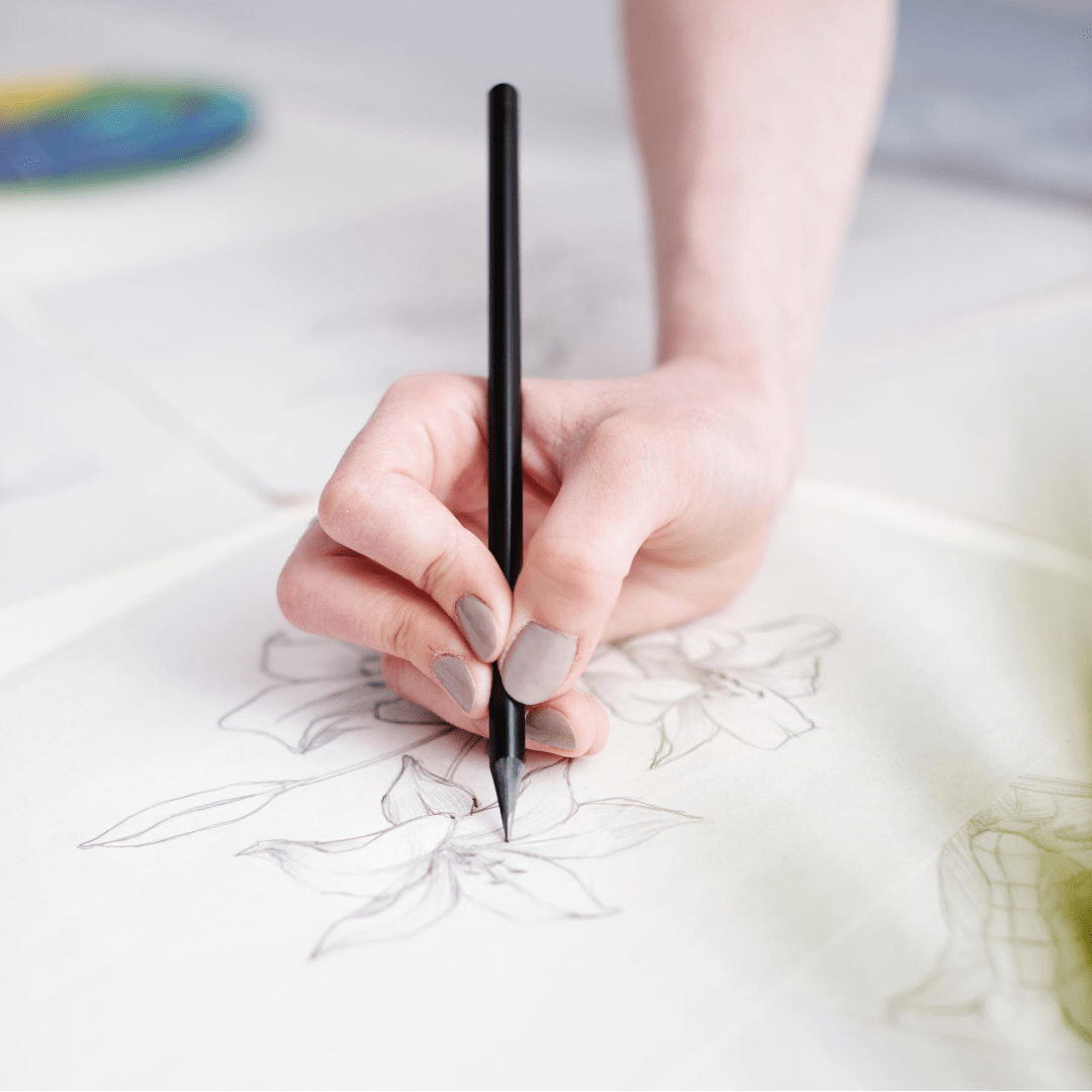 hand of a female artist drawing a flower with a black charcoal pencil