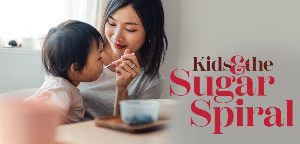 Title: Kids and the sugar spiral. Image of a mom feeding fruit to a toddler with a spoon